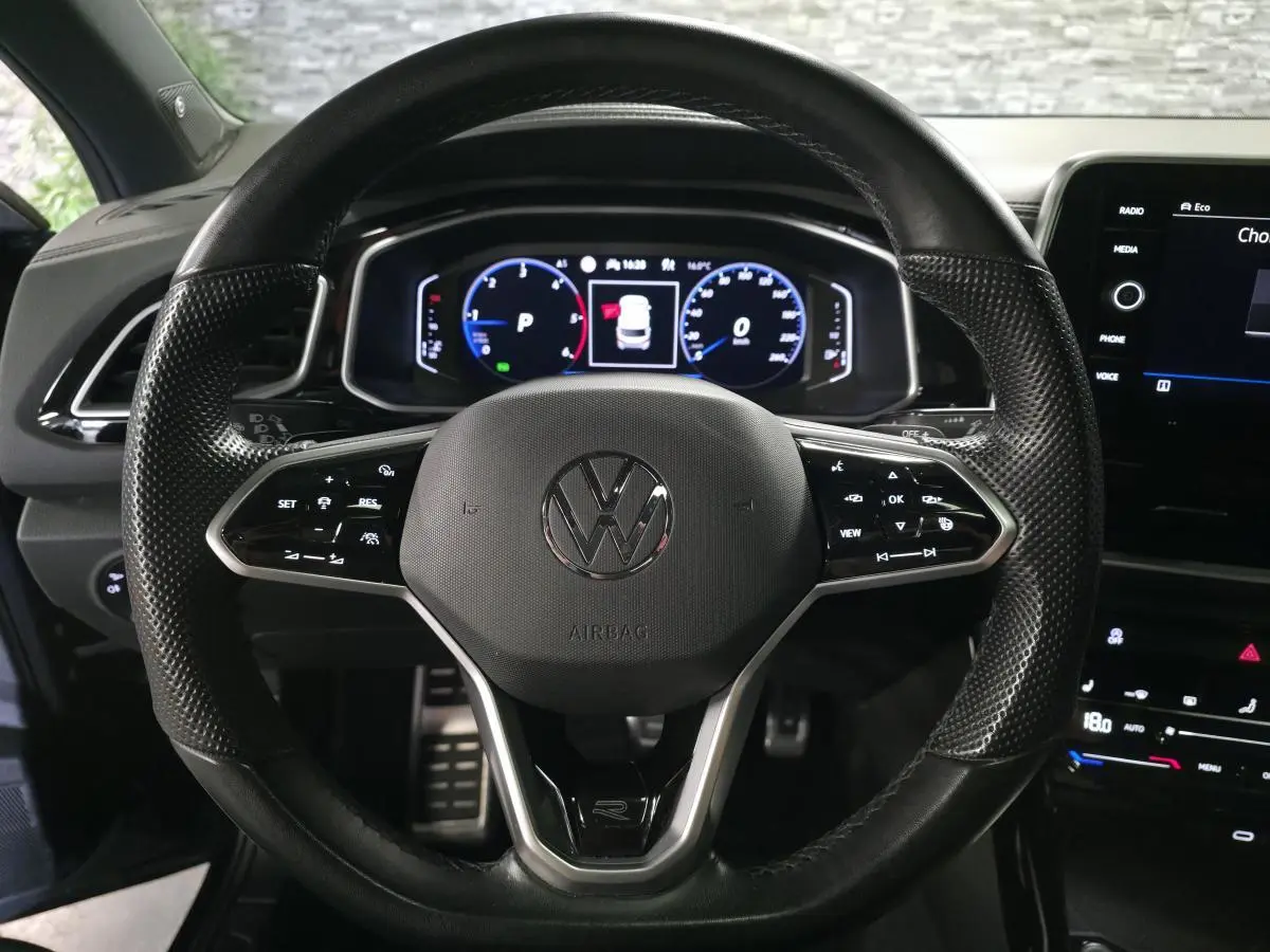 Vue rapprochée du volant en cuir noir avec logo Volkswagen et tableau de bord digital du T-Roc 2023.