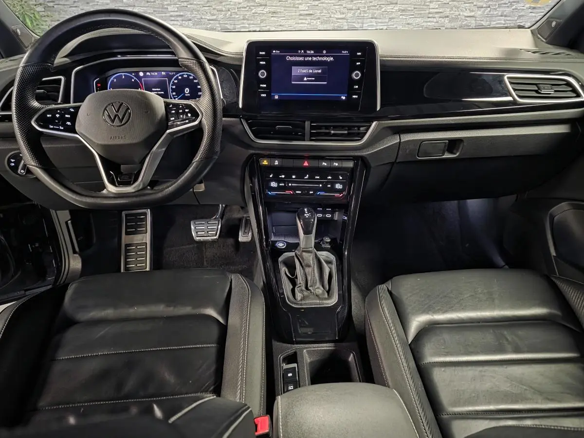Vue intérieure avant du Volkswagen T-Roc 2.0 TDI noir, mettant en valeur le volant multifonction, l’écran tactile et la sellerie cuir R-Line.