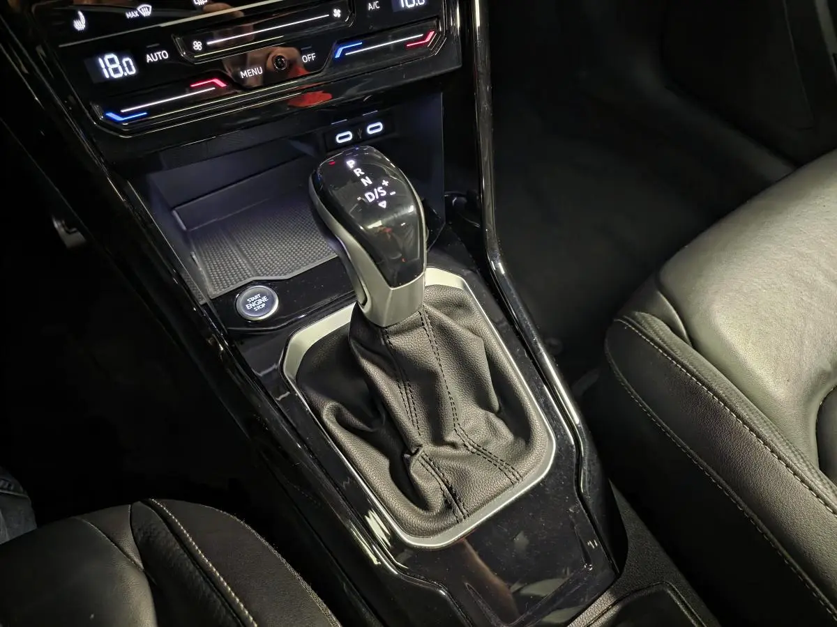 Gros plan sur la console centrale noire du Volkswagen T-Roc 2023 avec levier de vitesse automatique et sièges en cuir.