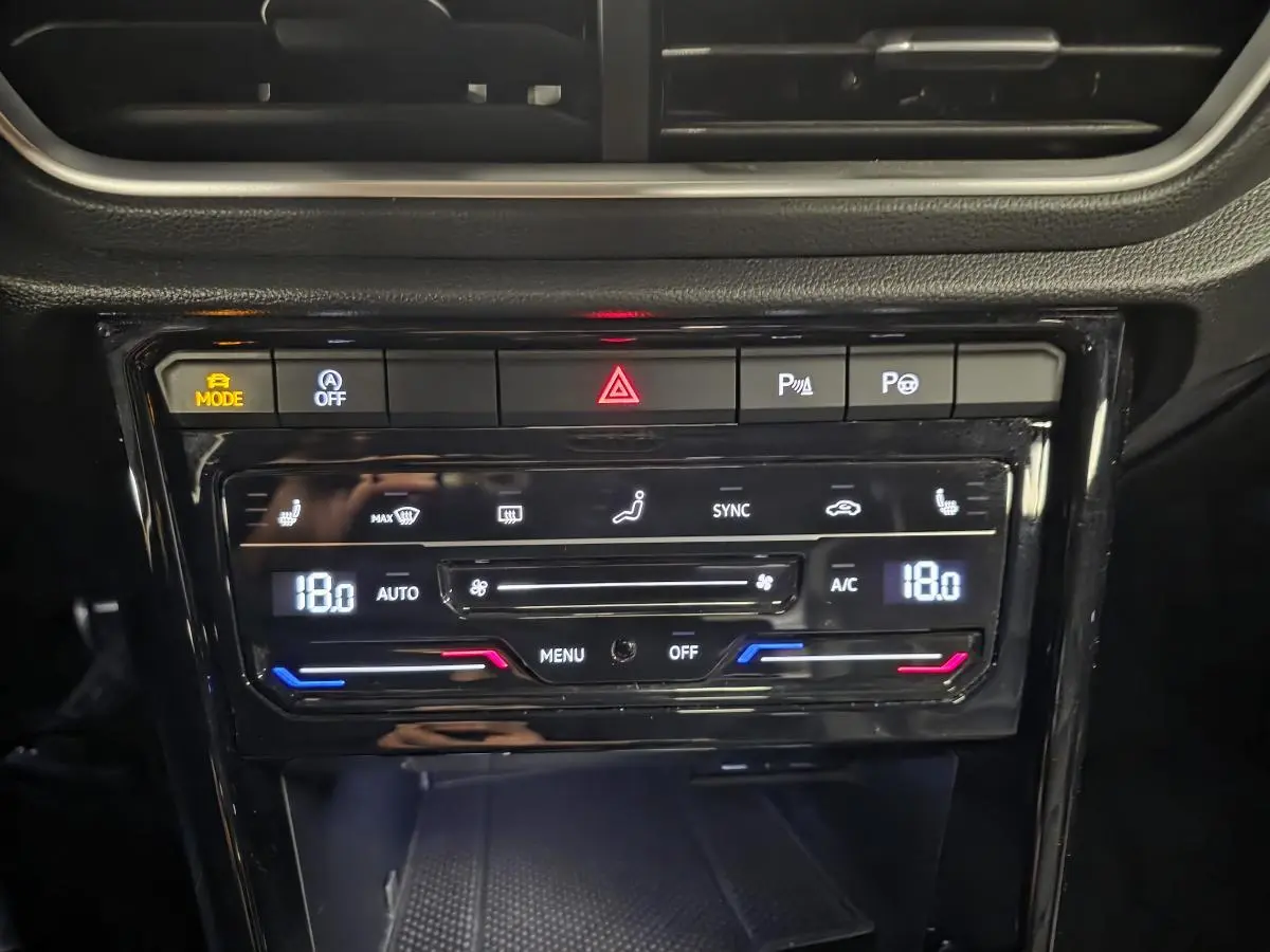 Vue rapprochée de la console centrale noire du Volkswagen T-Roc 2023 avec commandes de climatisation digitale et boutons de sécurité.