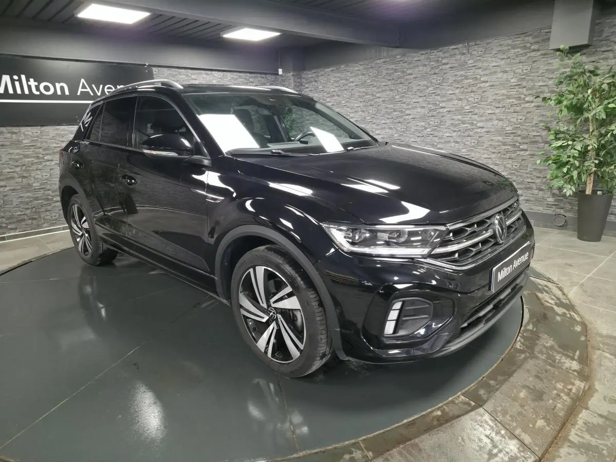 Volkswagen T-Roc noir en 3/4 avant droit, avec jantes alliage et calandre R-Line visible en showroom.