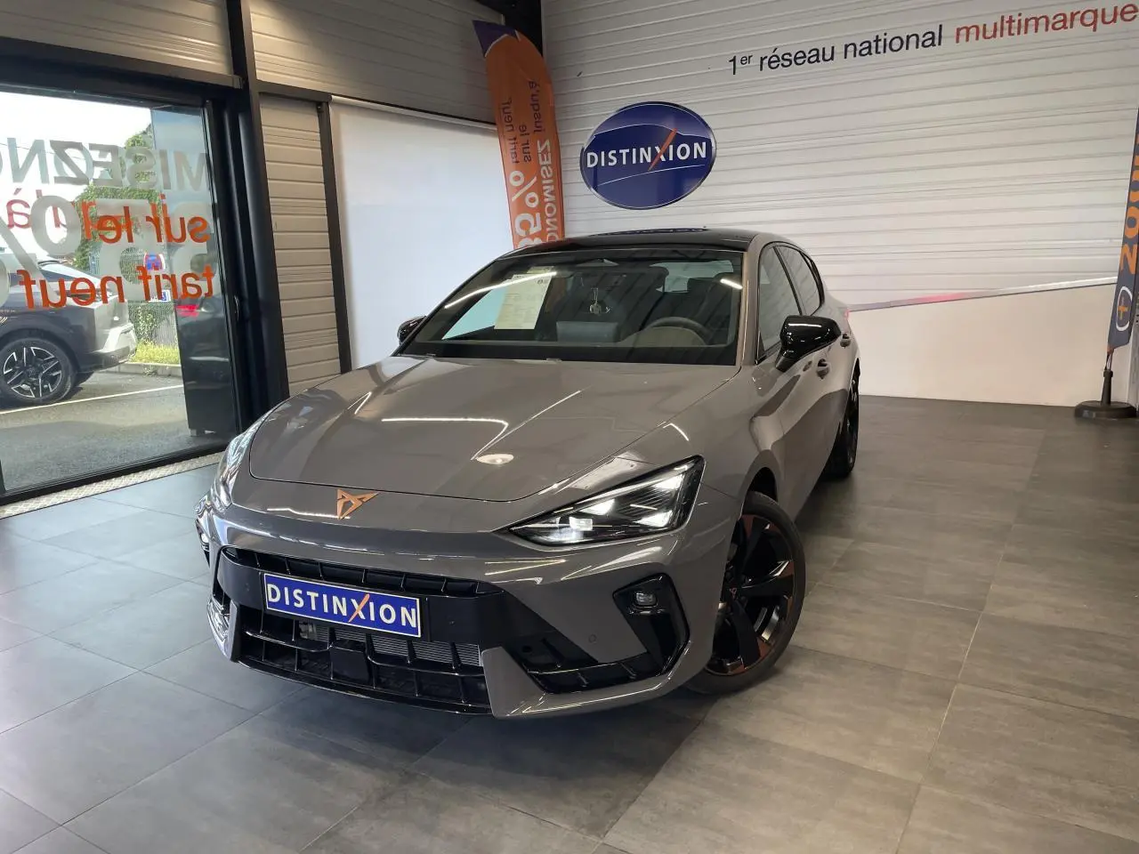 Vue 3/4 avant d'une CUPRA Leon gris magnétique avec jantes cuivrées et logo CUPRA sur le capot, en showroom.