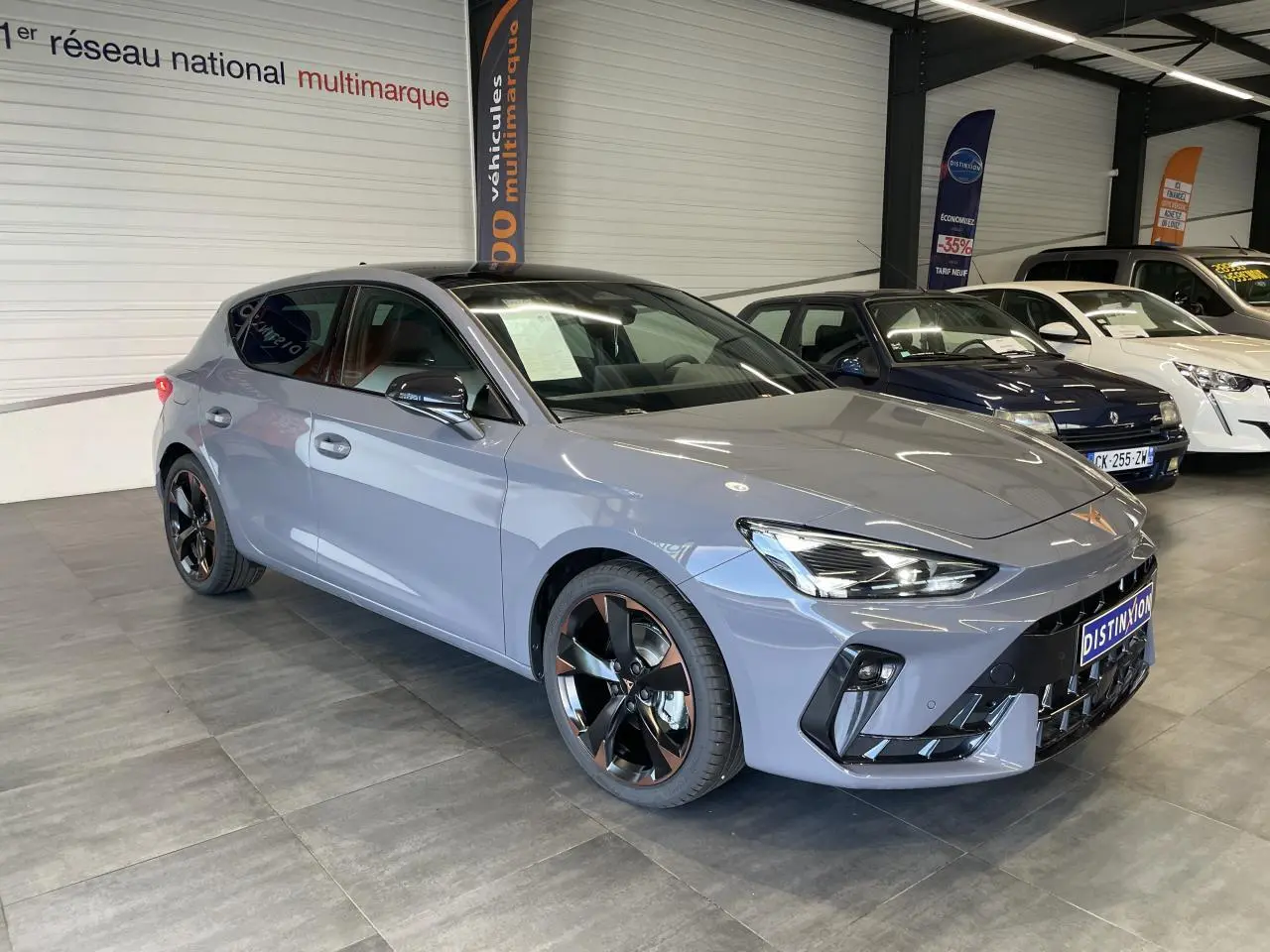Vue 3/4 avant d'une CUPRA Leon gris magnétique avec jantes alliage noires et cuivrées en showroom.
