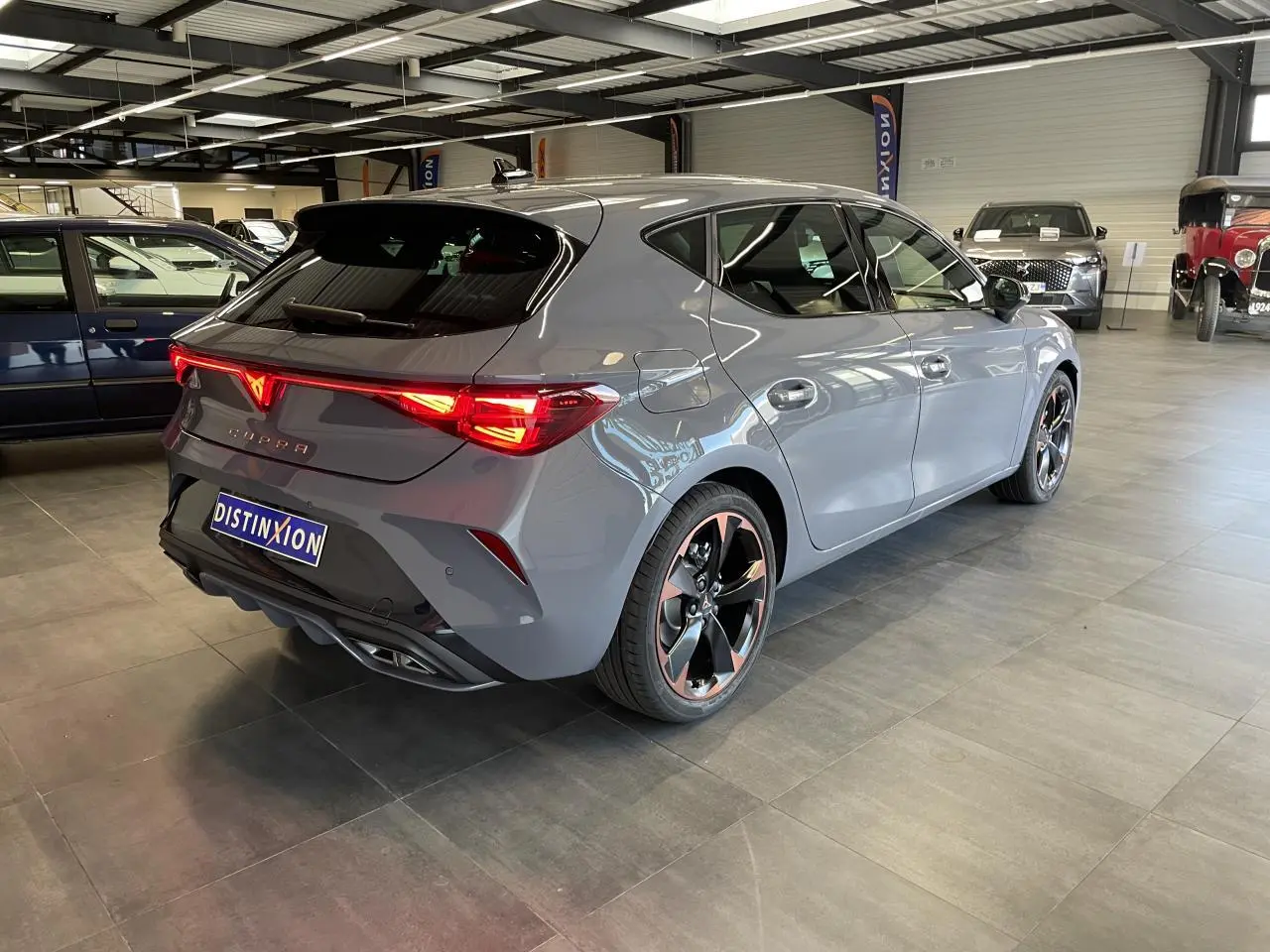 Vue 3/4 arrière droite d'une CUPRA Leon gris magnétique avec jantes alliage 18'' cuivrées et feux arrière Tri-LED allumés.
