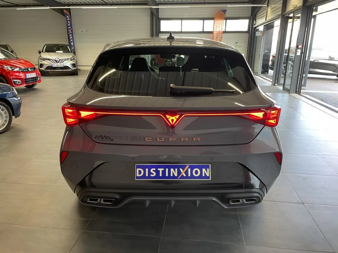 Vue arrière d'une CUPRA Leon gris magnétique avec bandeau lumineux et double sortie d'échappement stylisée.