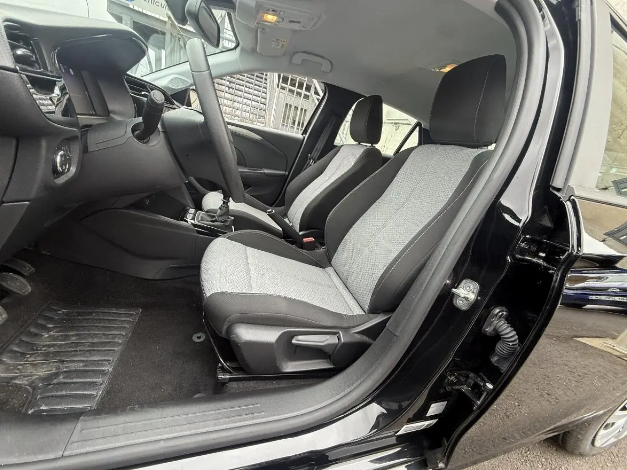 Vue intérieure côté conducteur de l’Opel Corsa 2025 noir karbon, montrant les sièges avant gris et la boîte manuelle.