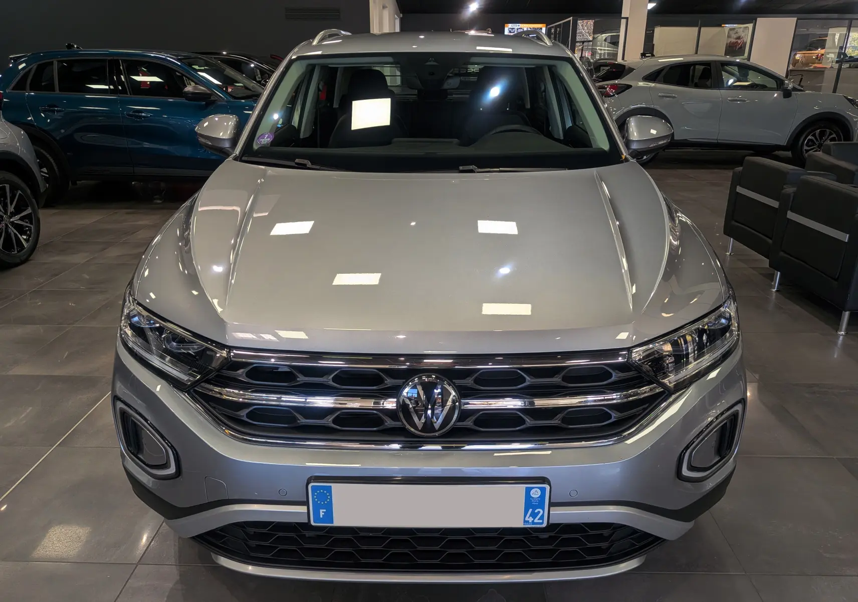 Vue frontale d'un Volkswagen T-Roc 1.5 TSI gris pyrite, mettant en valeur sa calandre chromée et ses phares LED.
