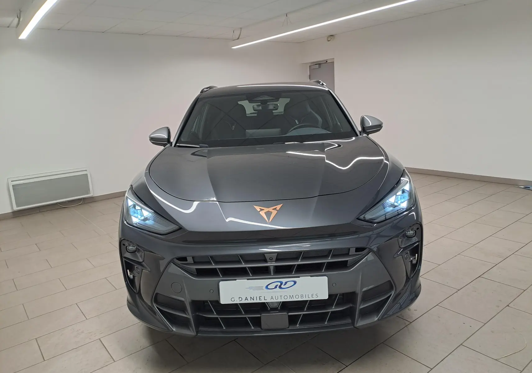 Vue frontale du CUPRA TERRAMAR gris Timanfaya avec feux allumés et logo cuivré sur le capot.