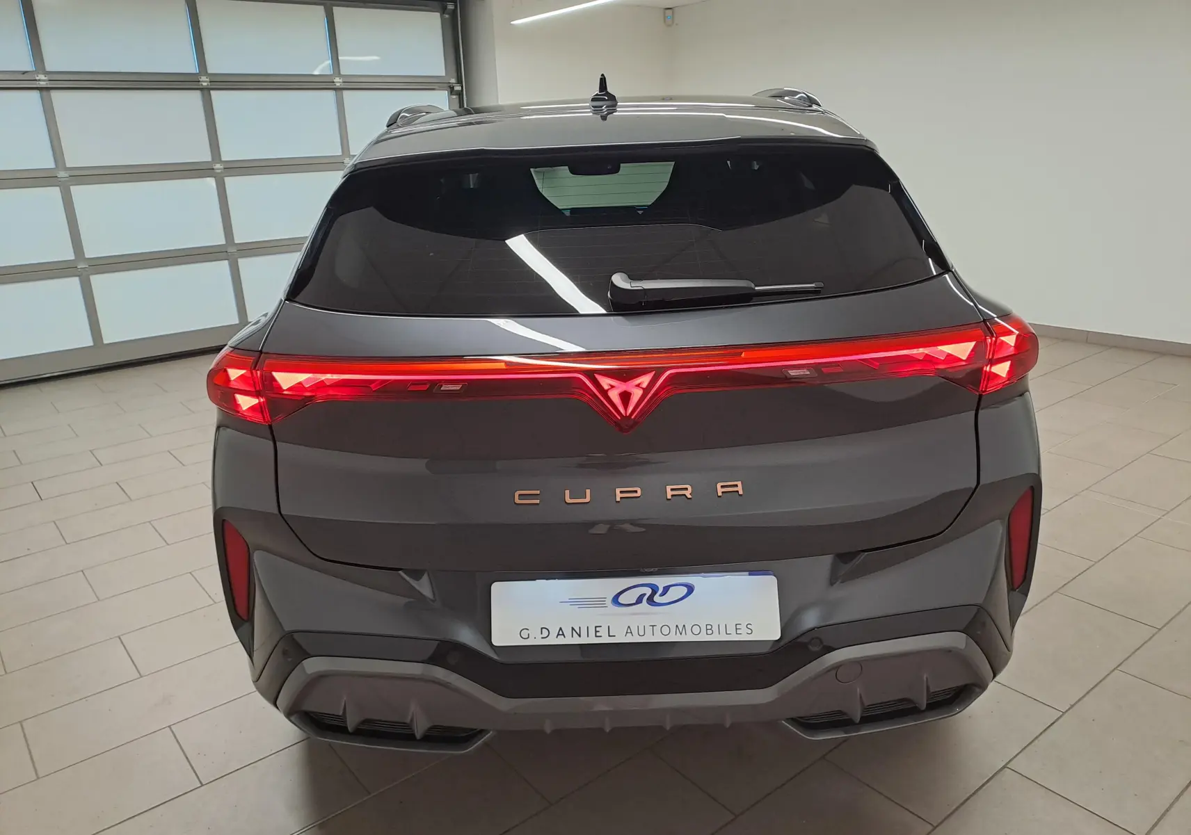 Vue arrière du CUPRA TERRAMAR gris Timanfaya avec feux arrière allumés et logo lumineux au centre.