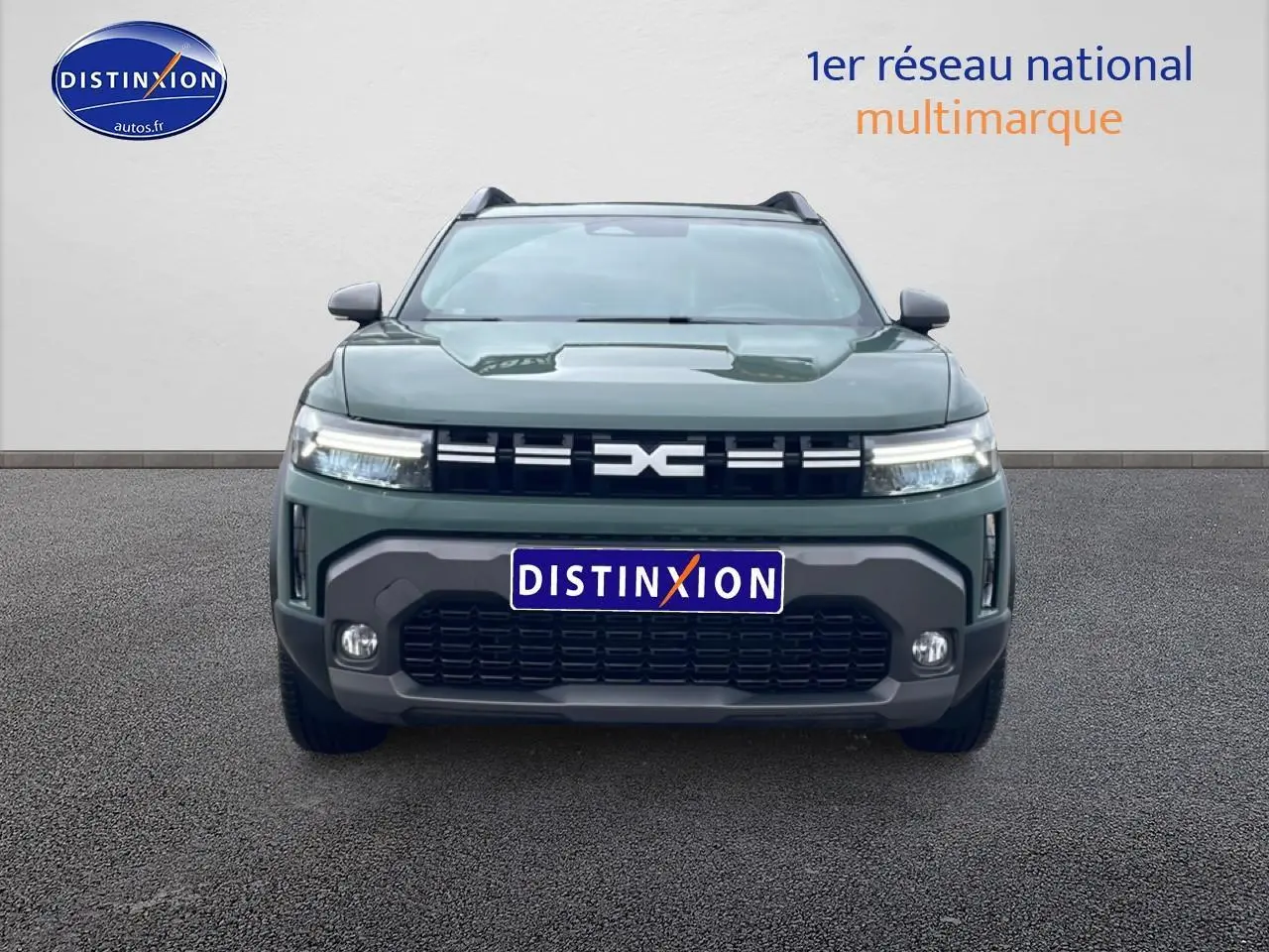 Vue frontale d'un Dacia Duster 2026 vert kaki avec calandre noire et phares LED allumés sur fond neutre.