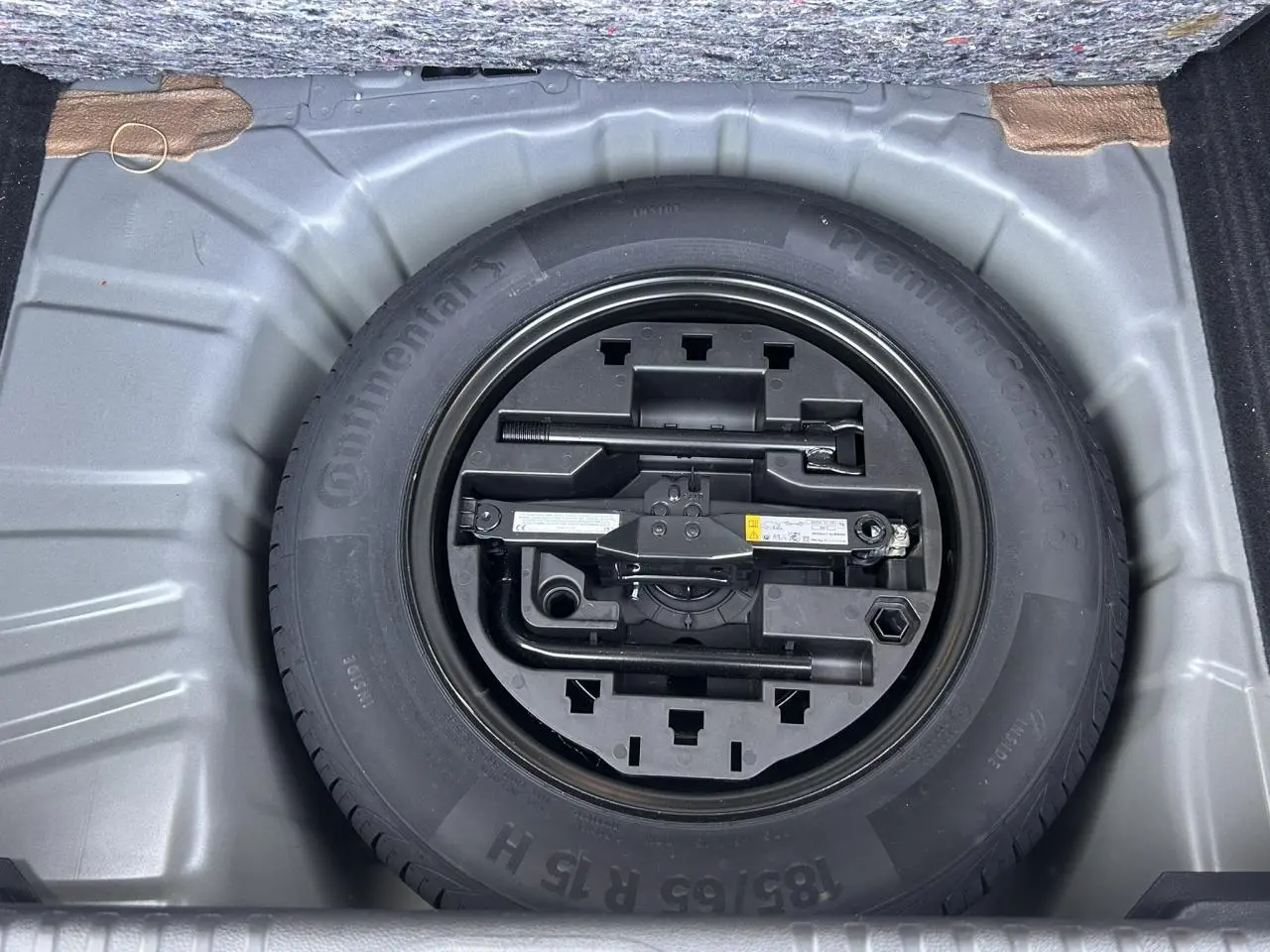 Vue plongeante sur la roue de secours tôle noire et son kit d'outils dans le coffre de la Renault Clio Noir Étoilé 2025.