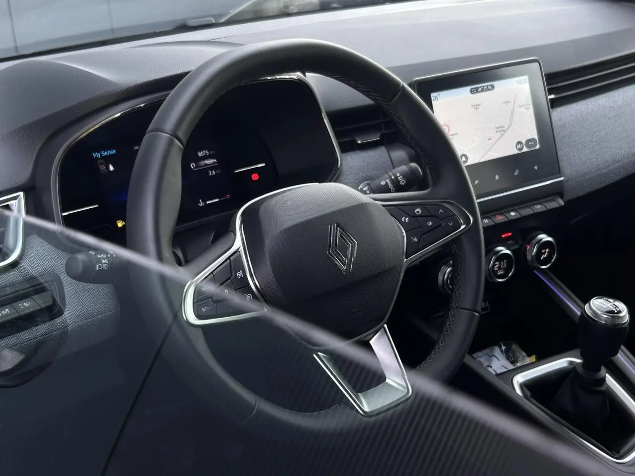 Vue intérieure côté conducteur de la Renault Clio noire étoilé 2025, volant multifonction et écran tactile central visibles.
