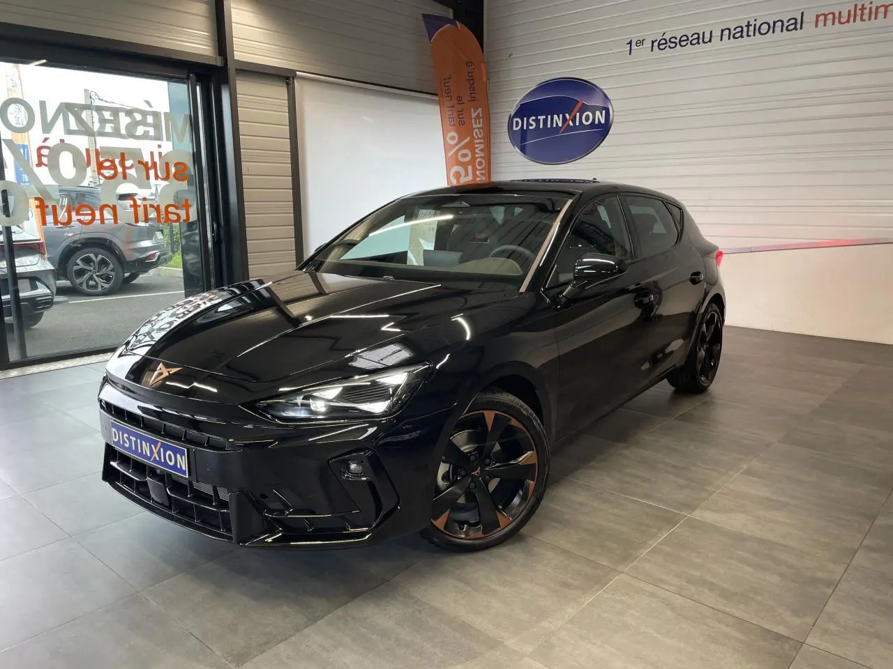 Vue 3/4 avant droite d'une CUPRA Leon noire avec jantes alliage noires et cuivrées, dans un showroom intérieur.