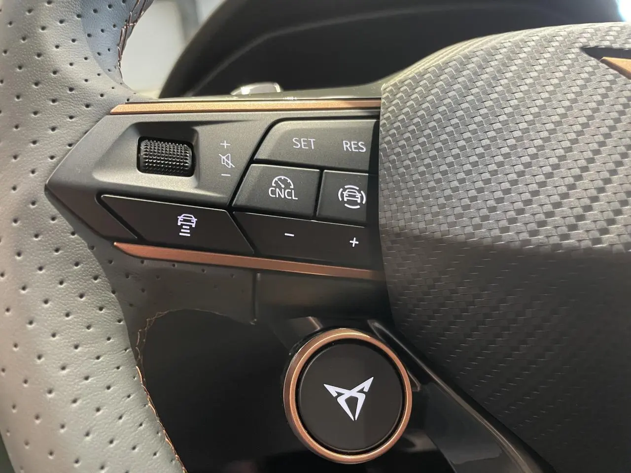 Gros plan sur le volant perforé noir avec boutons de commande et logo CUPRA cuivré au centre.