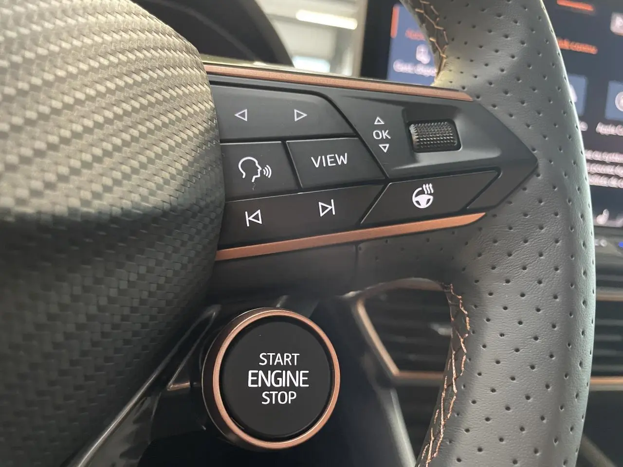 Gros plan sur le volant perforé noir avec surpiqûres cuivrées et bouton Start Engine Stop de la CUPRA Leon 2026.
