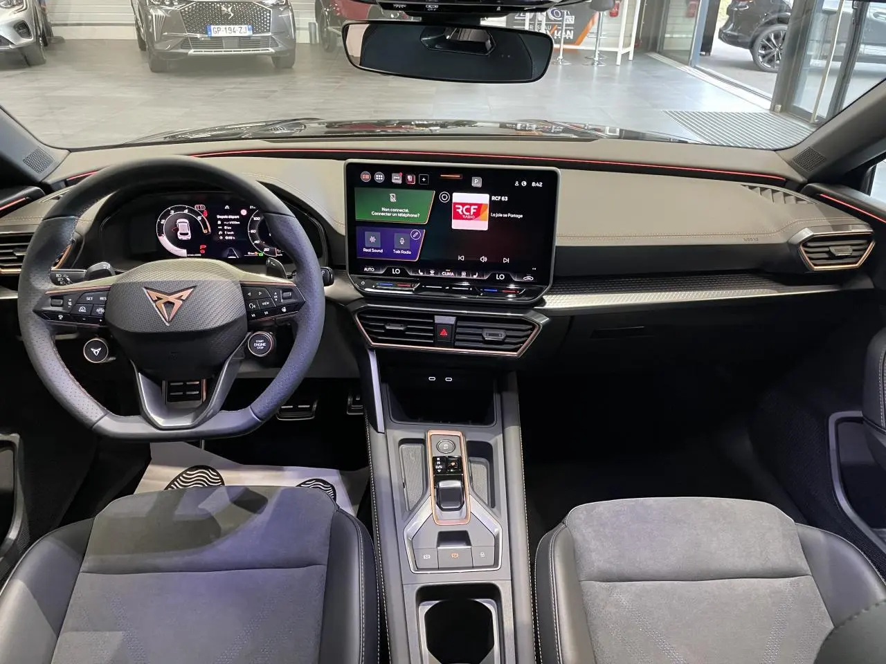 Vue intérieure avant de la CUPRA Leon 2026, tableau de bord noir avec volant sport et écran tactile central.