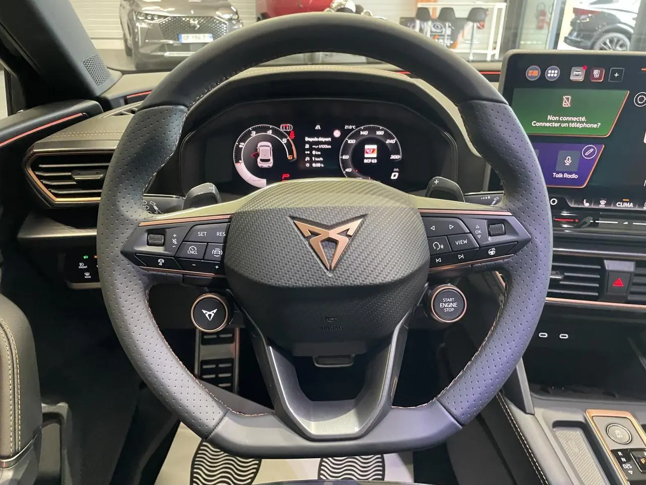 Vue rapprochée du volant cuir perforé noir avec logo Cupra cuivré et tableau de bord digital lumineux.