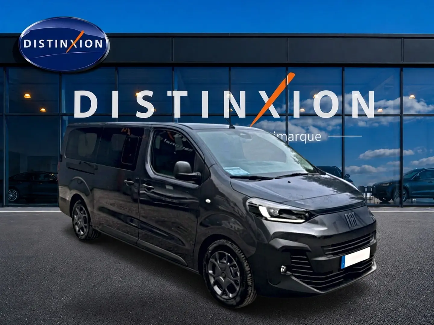 Fiat Scudo Combi gris titane en 3/4 avant droit, porte latérale coulissante visible, devant vitrine Distinxion.