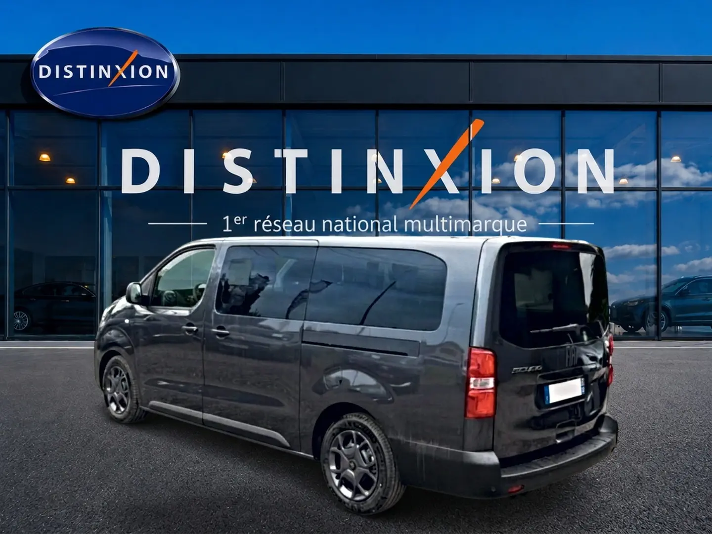 Vue 3/4 arrière droite d'un FIAT Scudo Combi gris titane avec porte latérale coulissante, stationné devant un showroom Distinxion.