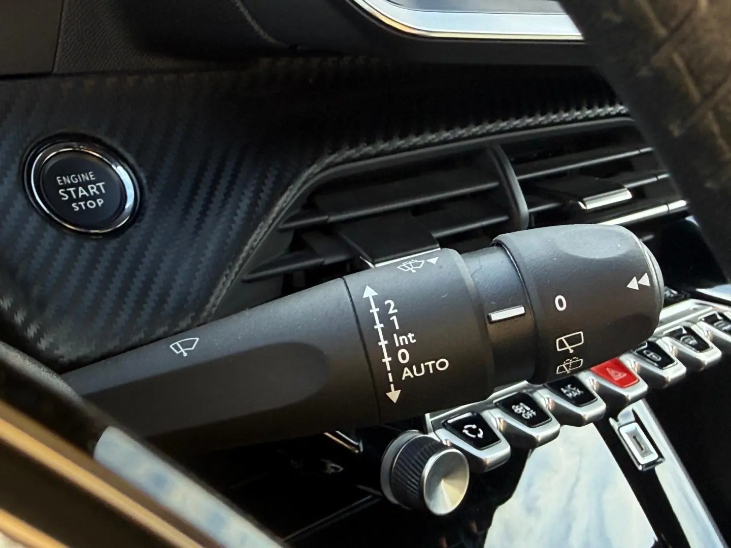 Gros plan sur le commodo d’essuie-glace et le bouton start/stop dans l’habitacle noir du Peugeot e-2008 2025.