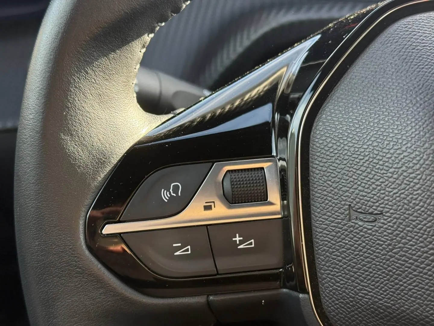 Gros plan sur les commandes gauche du volant noir du Peugeot e-2008 2025, avec boutons de volume et commande vocale.