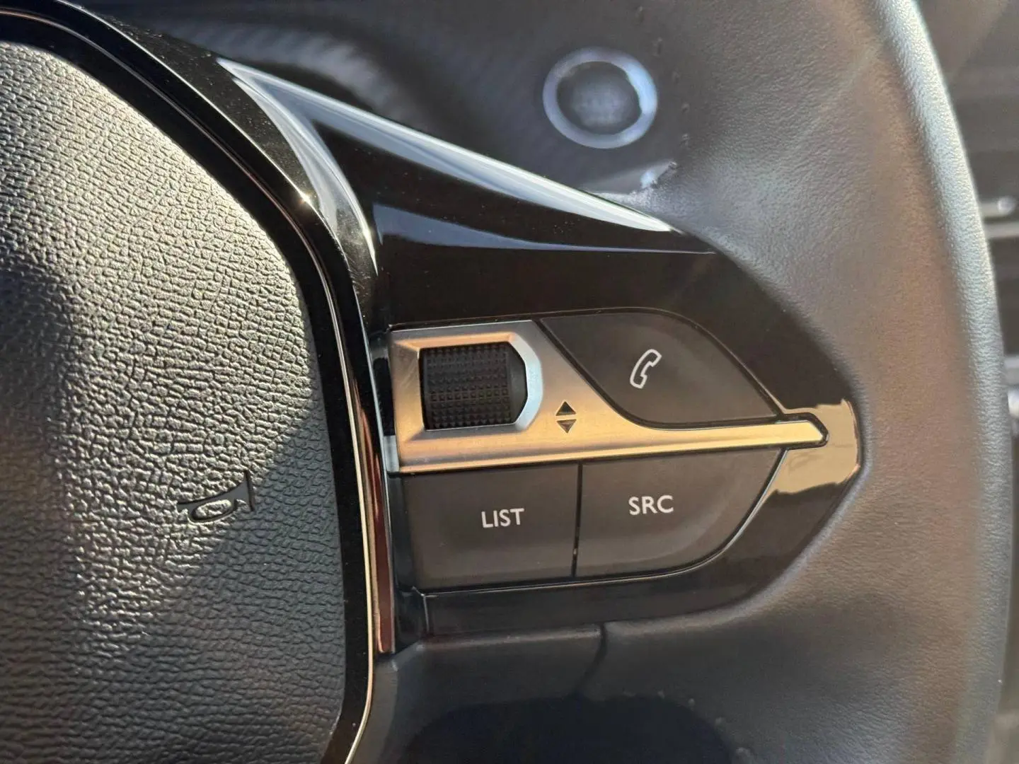 Gros plan sur les commandes gauche du volant noir du Peugeot e-2008 2025 avec boutons téléphone et réglages audio.
