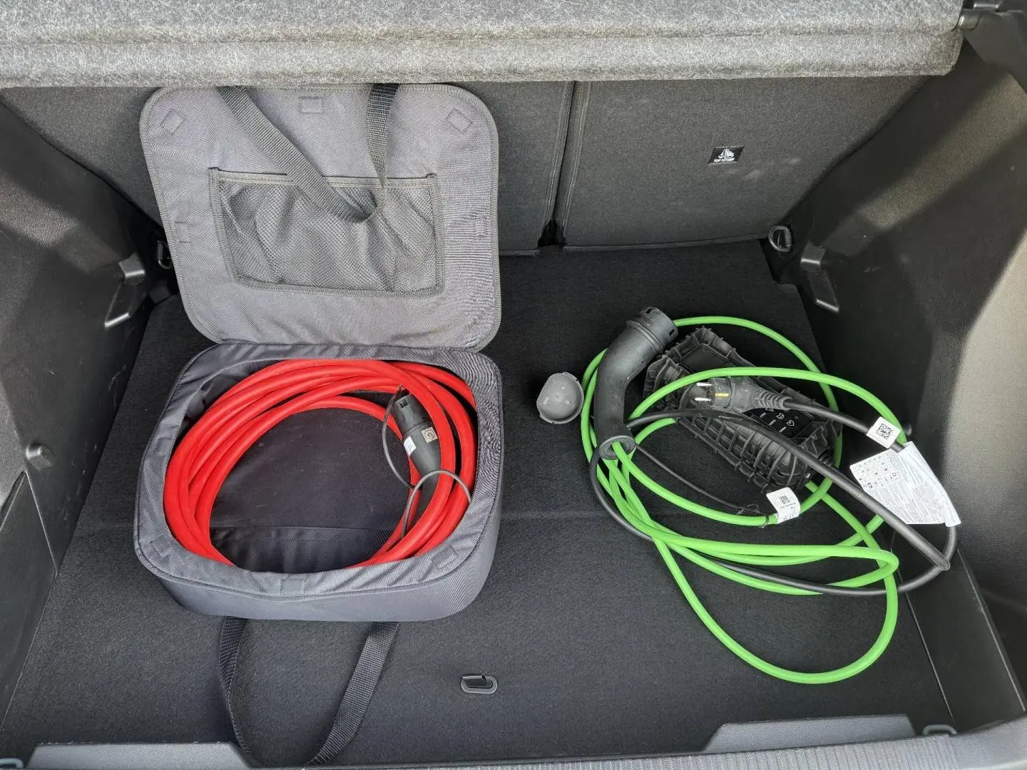 Coffre ouvert du Peugeot e-2008 2025 Bleu Obsession avec câbles de recharge électrique rouge et vert rangés.
