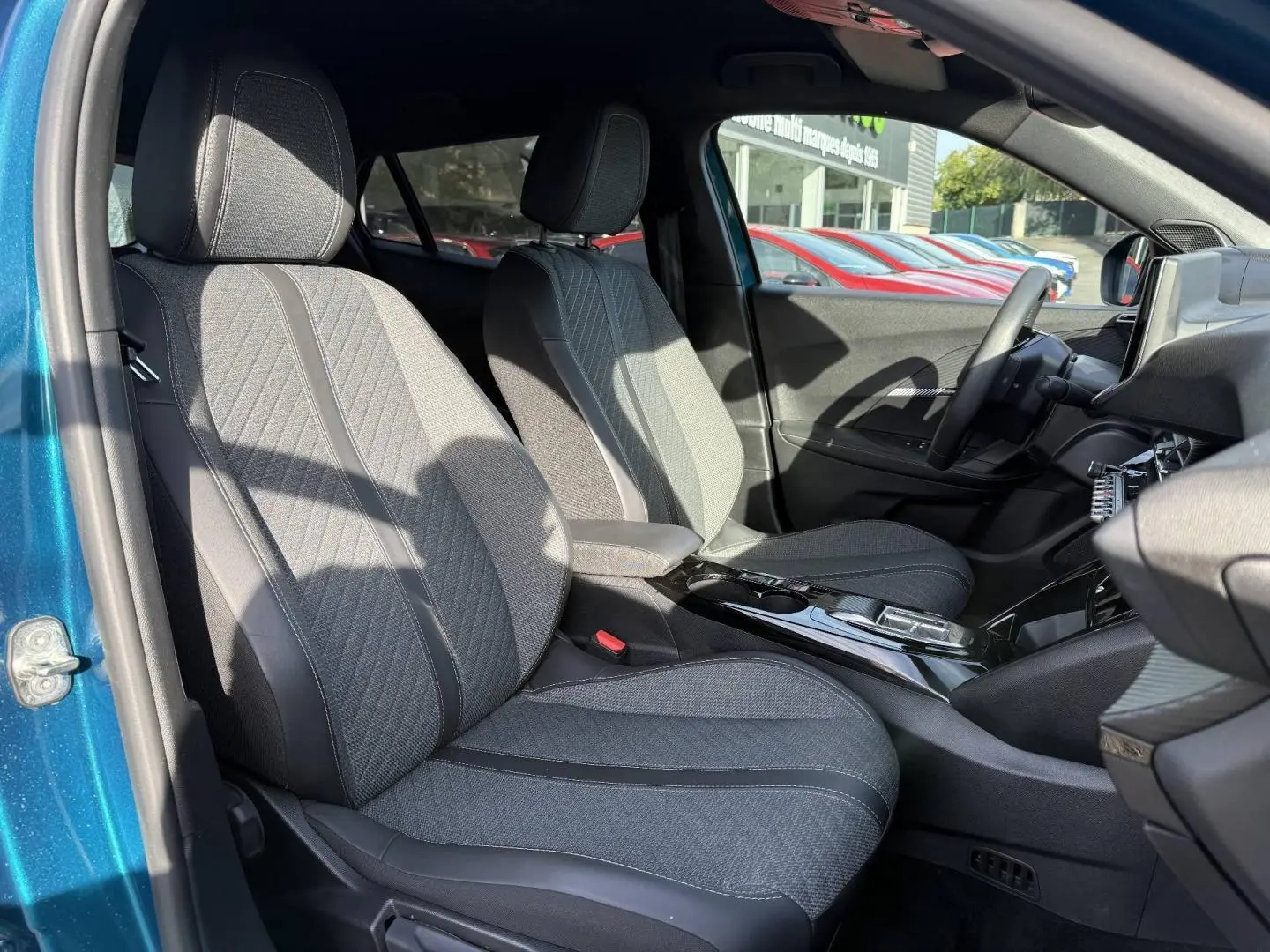 Vue intérieure côté gauche du Peugeot e-2008 2025 Bleu Obsession, montrant les sièges avant en tissu gris et la console centrale.