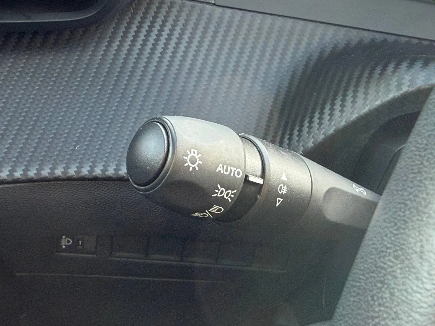 Gros plan sur la commande des phares automatiques dans l’habitacle du Peugeot e-2008 bleu Obsession.