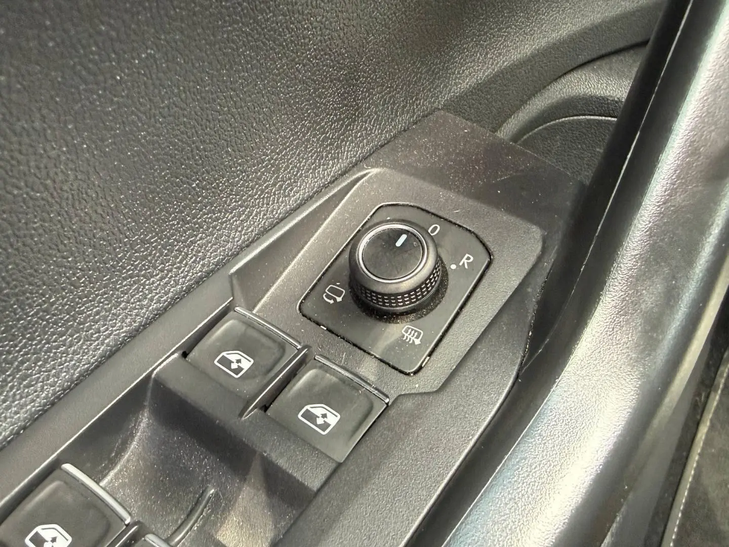 Vue rapprochée des commandes de réglage des rétroviseurs et des vitres sur la porte côté conducteur d’un Volkswagen Taigo gris.
