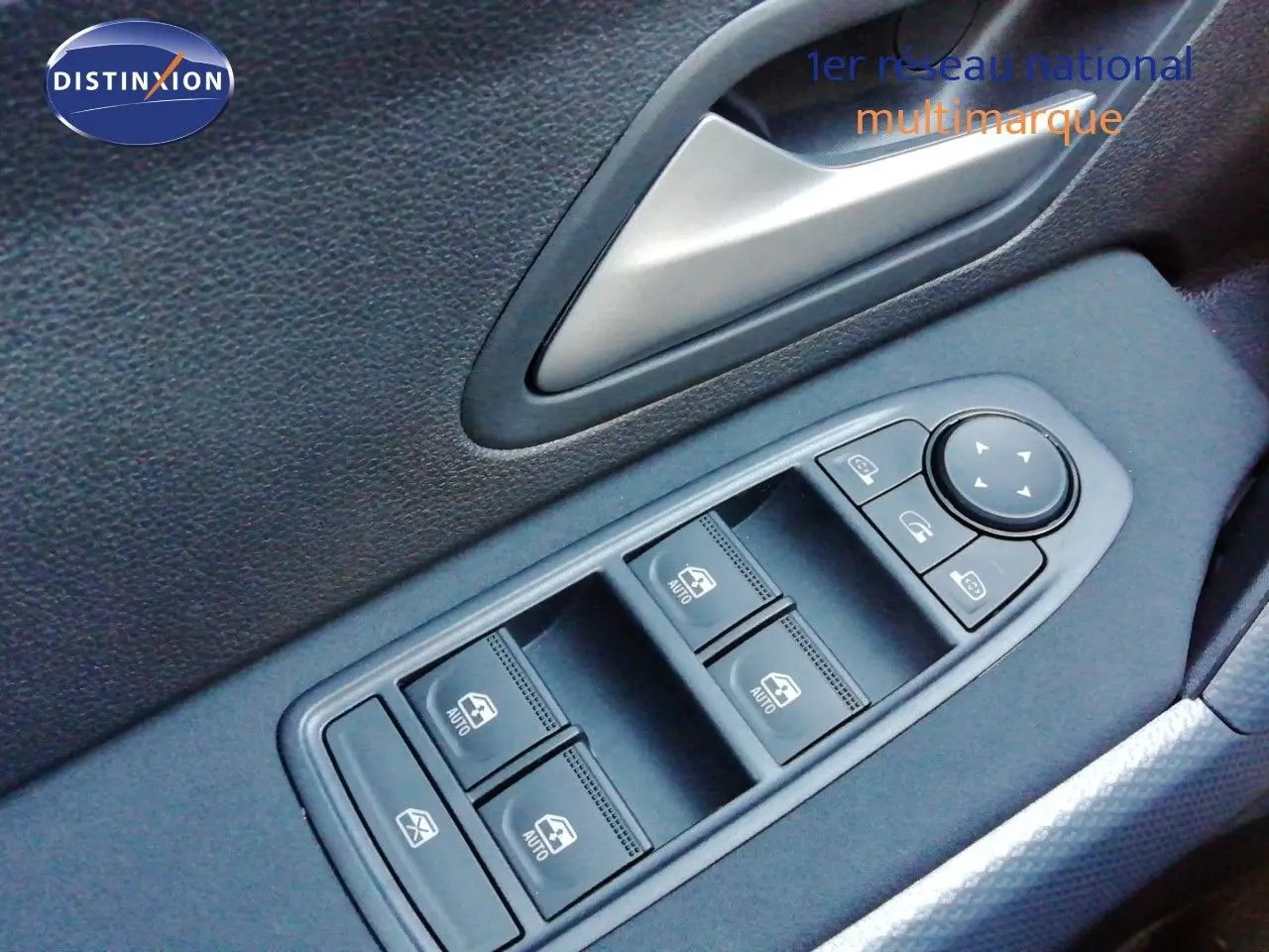 Gros plan sur les commandes des vitres électriques et rétroviseurs côté conducteur d’un Dacia Duster gris schiste métal.