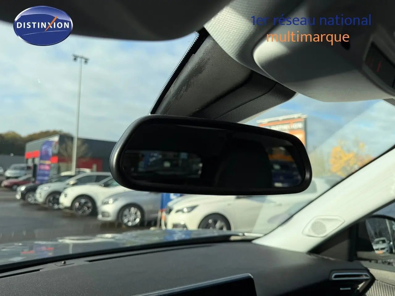 Vue intérieure centrée sur le rétroviseur intérieur d'une Peugeot 2008 gris Artense, avec vue floue sur des voitures blanches à l'extérieur.