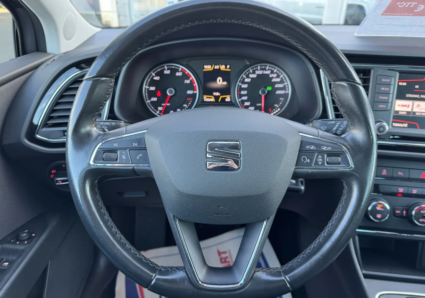 Vue rapprochée du volant en cuir noir d'une SEAT Leon 2016 avec tableau de bord et écran multimédia visibles.