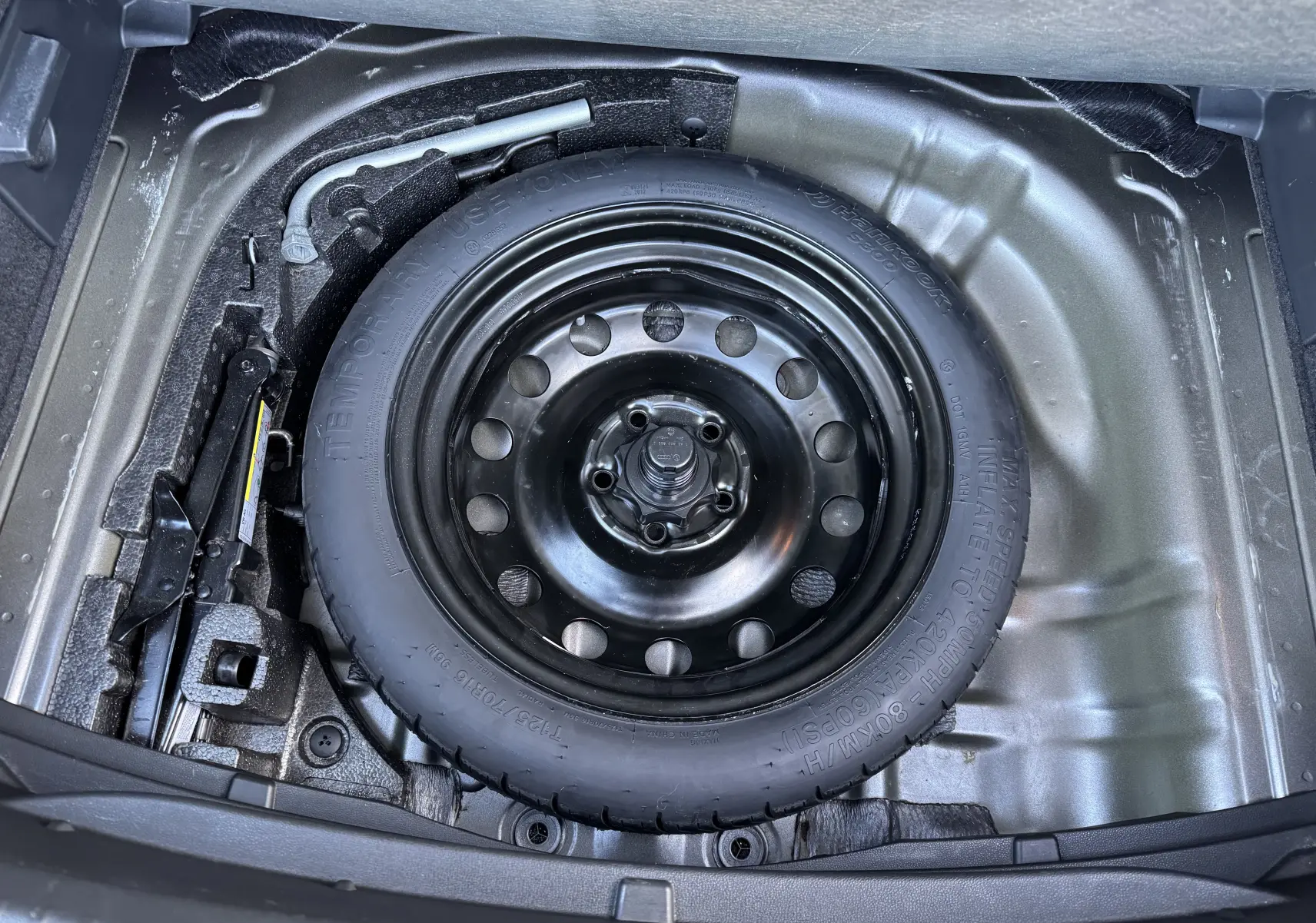 Vue plongeante sur la roue de secours noire et les outils de bord dans le coffre d'un SEAT Leon gris 2016.