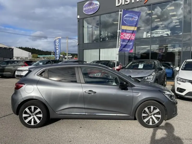 Profil côté gauche d'une Renault Clio V TCE 90 X-TRONIC Evolution gris foncé métal stationnée devant un concessionnaire.