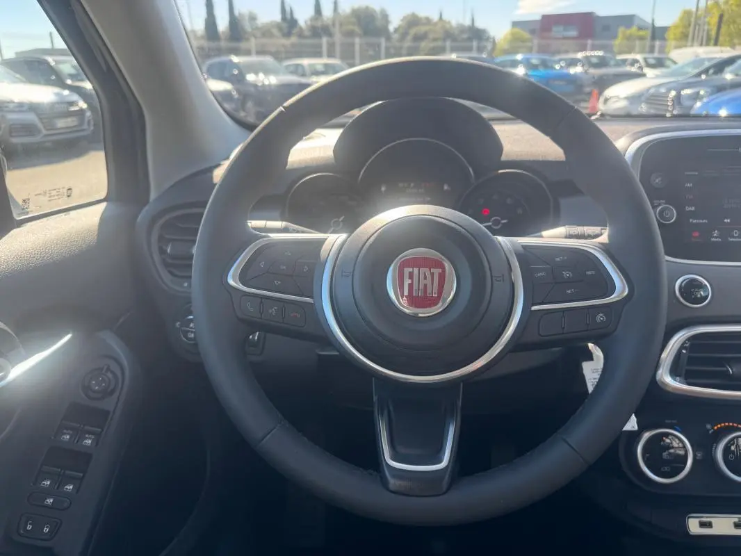 Vue centrée sur le volant du Fiat 500X 2024, avec tableau de bord et commandes visibles en intérieur.