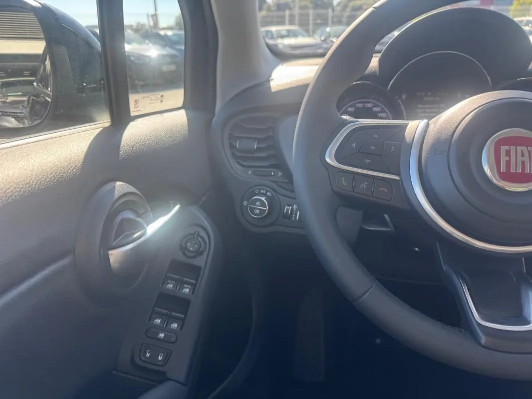 Vue intérieure côté gauche du volant du Fiat 500X bleu, montrant commandes de vitres et volant avec logo FIAT.