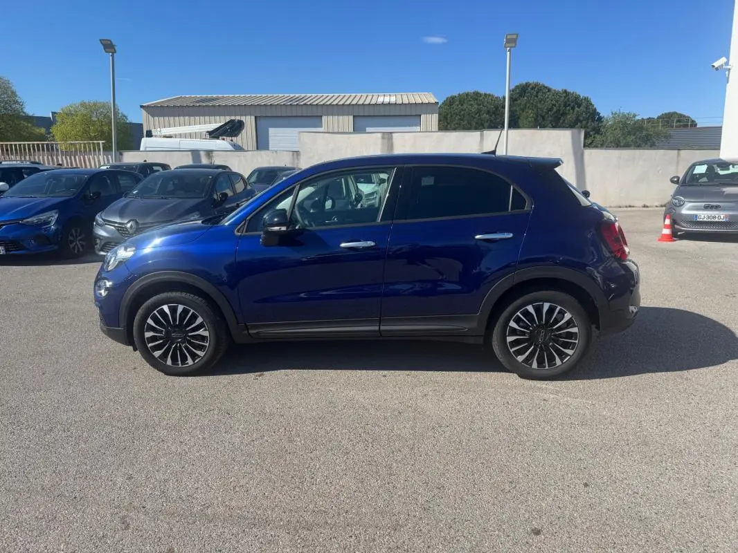 Profil droit d'un FIAT 500X bleu 2024 avec jantes classiques 16 pouces sur un parking en extérieur.