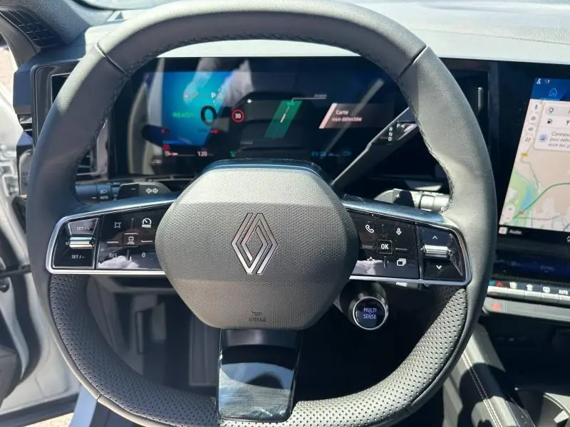 Vue rapprochée du volant multifonction noir du Renault Austral blanc nacré avec écran numérique et écran tactile GPS en arrière-plan.