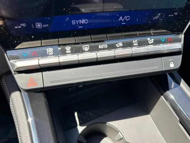 Gros plan sur la console centrale noire du Renault Austral blanc nacré, montrant les commandes de climatisation et d’alerte.