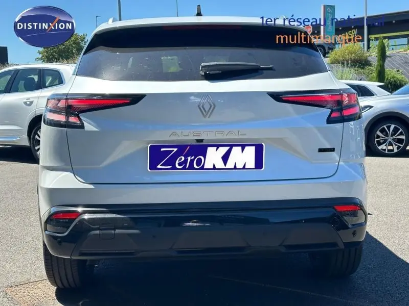 Vue arrière d'un Renault Austral blanc nacré brillant avec feux LED étirés et logo central sur un parking extérieur.