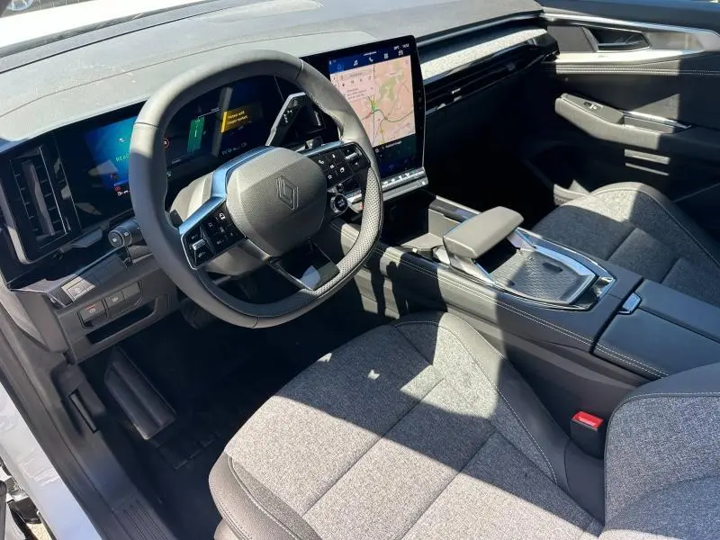 Intérieur Renault Austral 2025 vu côté conducteur, volant multifonction, écran tactile vertical et sièges tissu gris clair.
