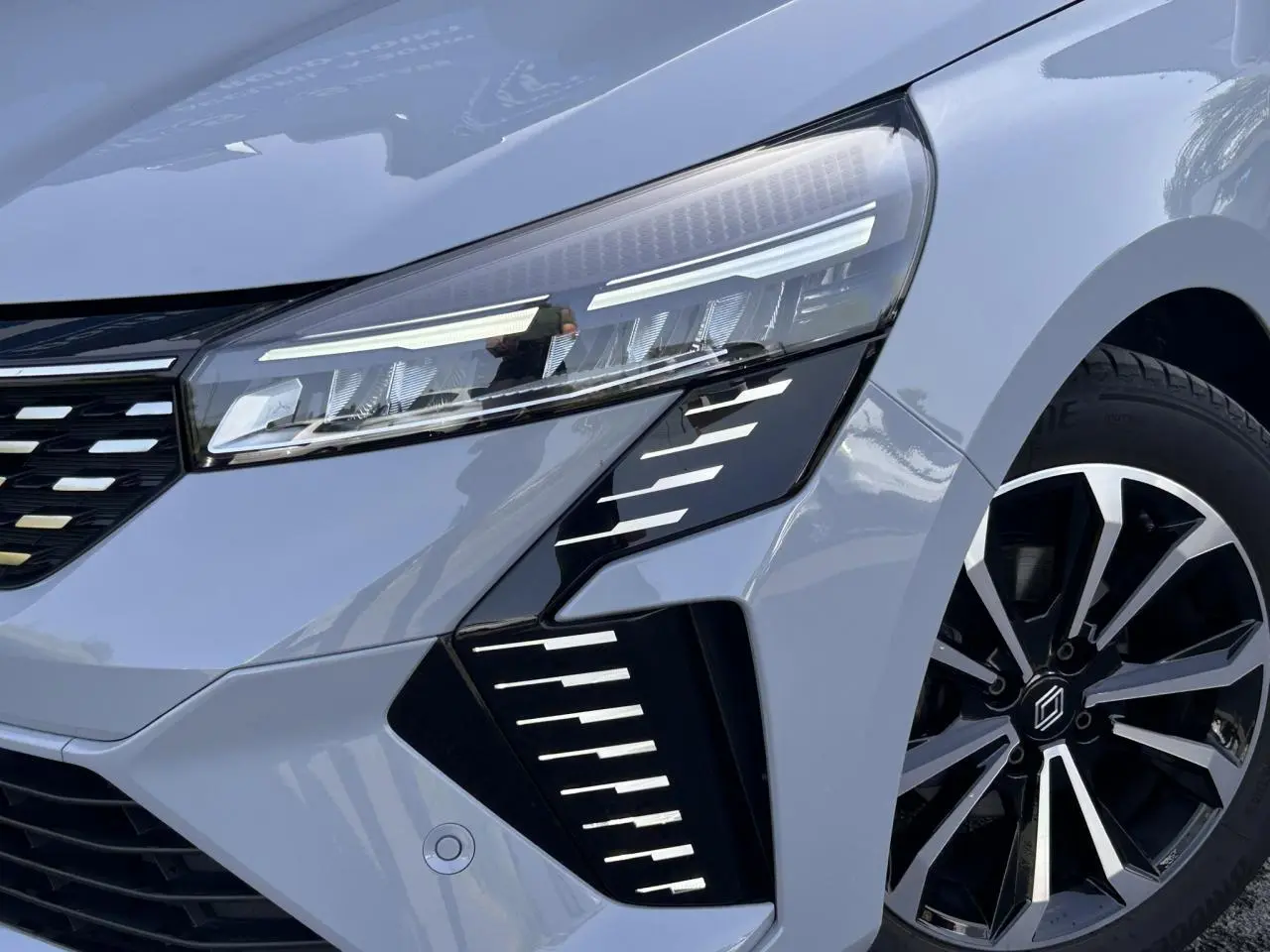 Gros plan sur l'avant droit de la Renault Clio 2025 Gris Rafale, mettant en valeur le phare LED et la jante alliage noire et argent.