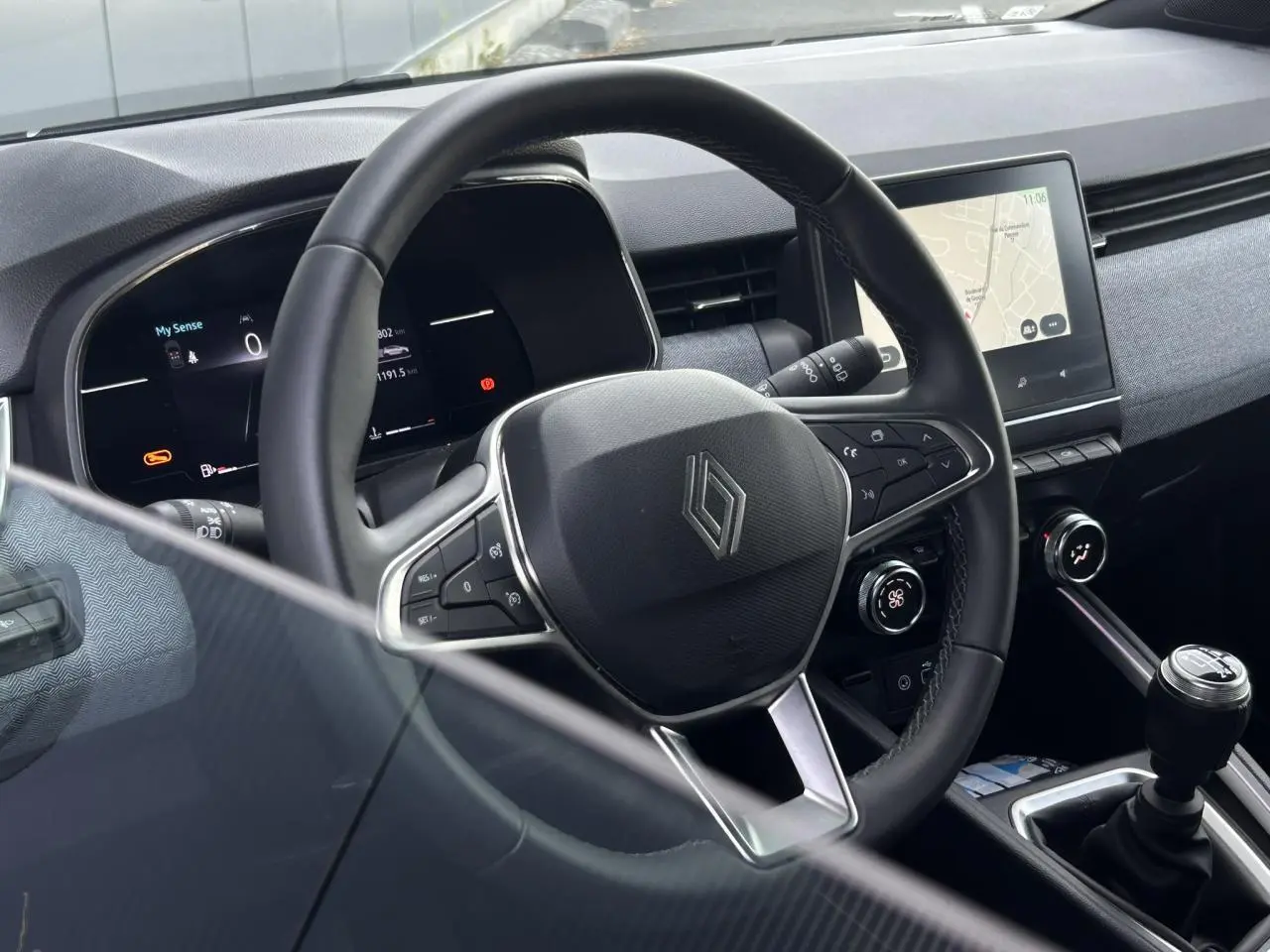 Intérieur de Renault Clio 2025, vue centrée sur le volant multifonction noir et la console avec écran tactile.