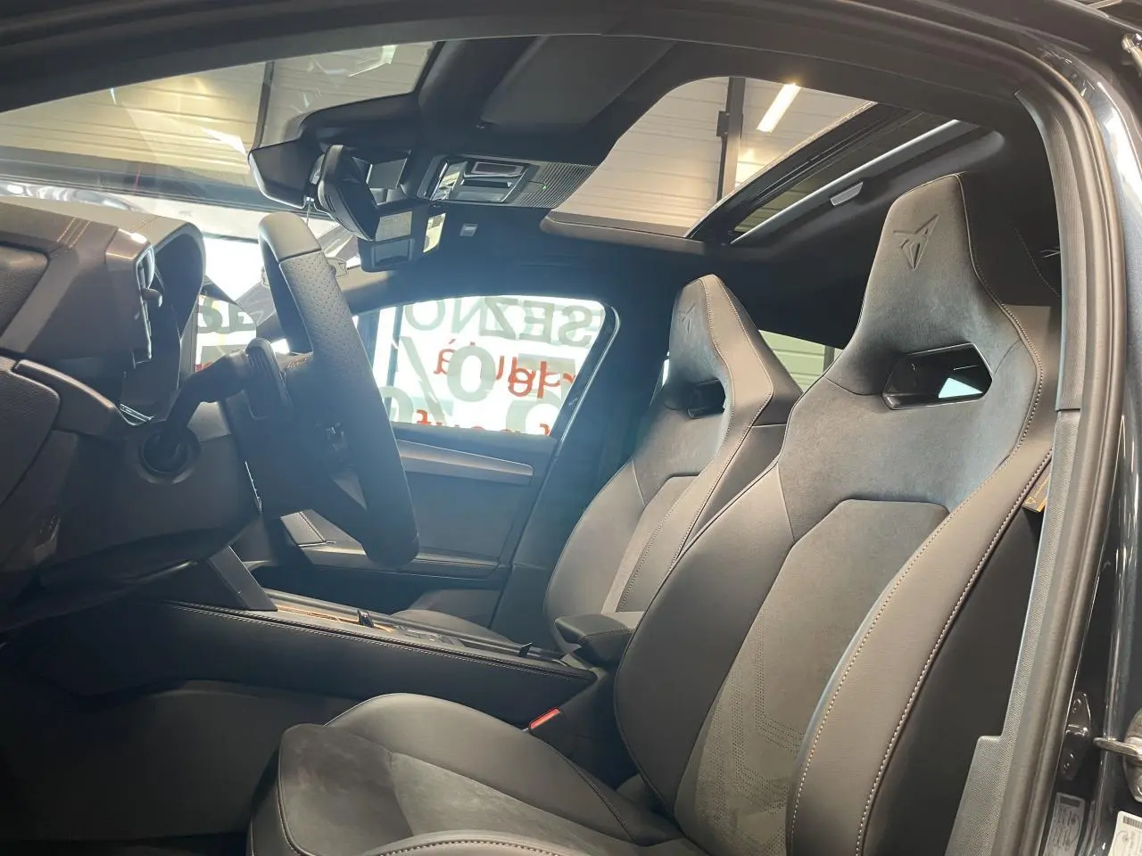 Vue intérieure côté conducteur de la CUPRA Leon 2026, sièges baquets noirs avec surpiqûres cuivrées et toit ouvrant panoramique.