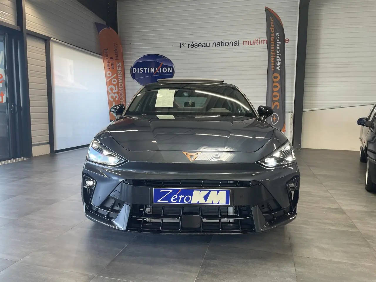 Vue avant d'une CUPRA Leon gris magnétique avec logo cuivré et phares LED allumés en showroom.