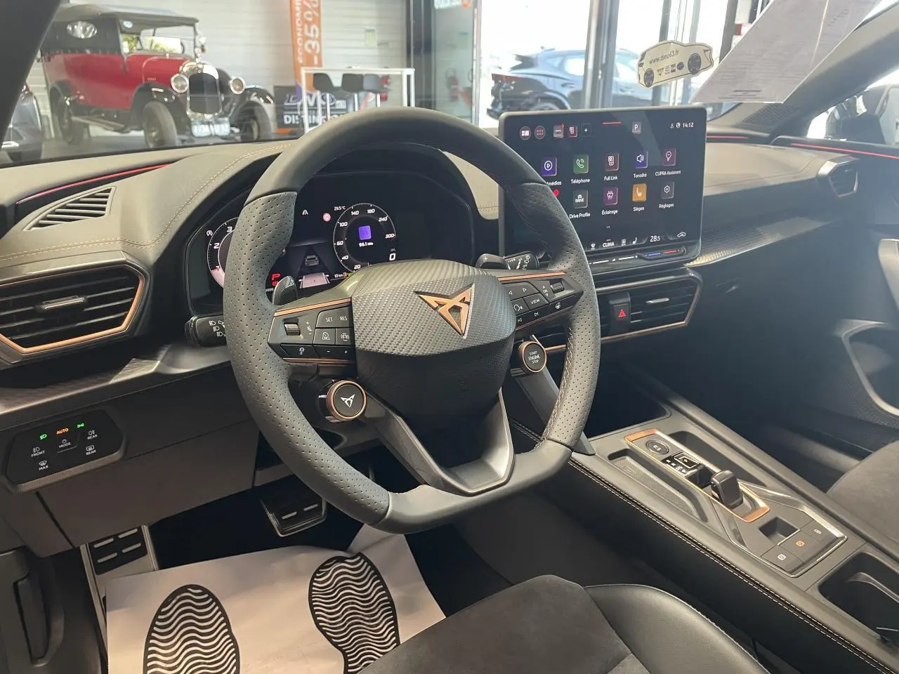 Vue intérieure du poste de conduite du CUPRA Leon gris, volant perforé avec logo cuivré et écran tactile central lumineux.