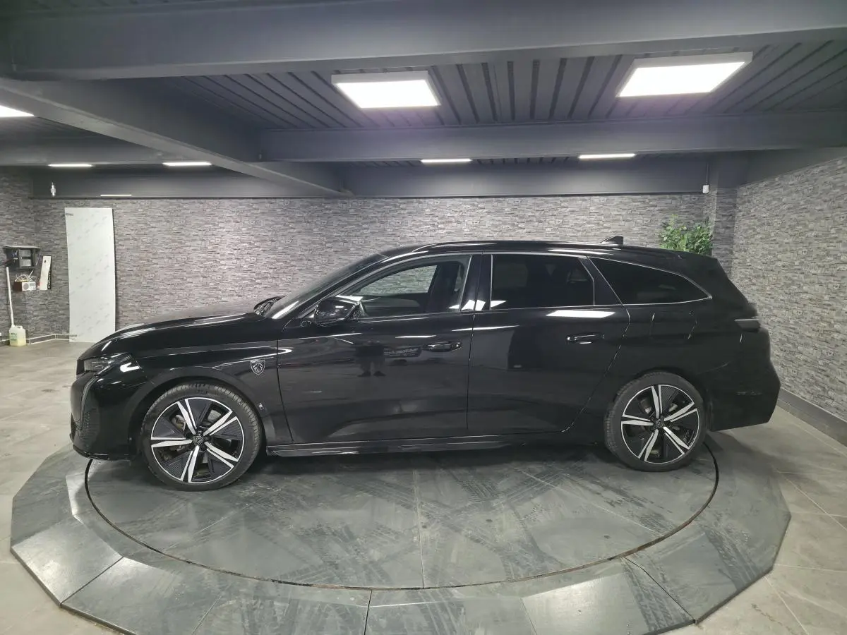 Peugeot 308 SW GT noire vue de profil côté gauche, jantes alliage 18'' et toit noir brillant en intérieur showroom.