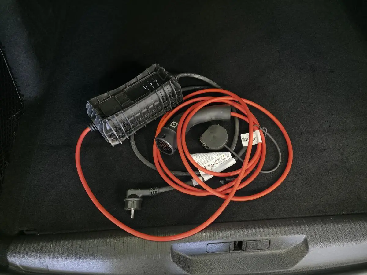 Câble de recharge hybride rouge et noir dans le coffre d'une Peugeot 308 SW noire, vue intérieure du coffre.