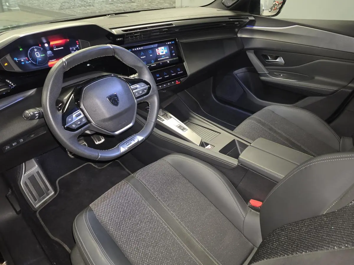 Vue intérieure côté conducteur de la Peugeot 308 SW GT 2024 noire, avec volant cuir, écran tactile et sellerie tri-matières.